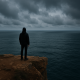 12 Znakova da se držite nečega kada to trebate pustiti | A person standing at the edge of a cliff, looking out at a vast ocean under a cloudy sky.